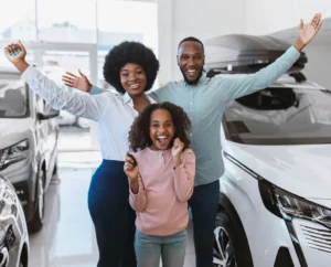 Happy Kenyan family celebrating a new car at a dealership, ready to choose between comprehensive and third-party insurance.